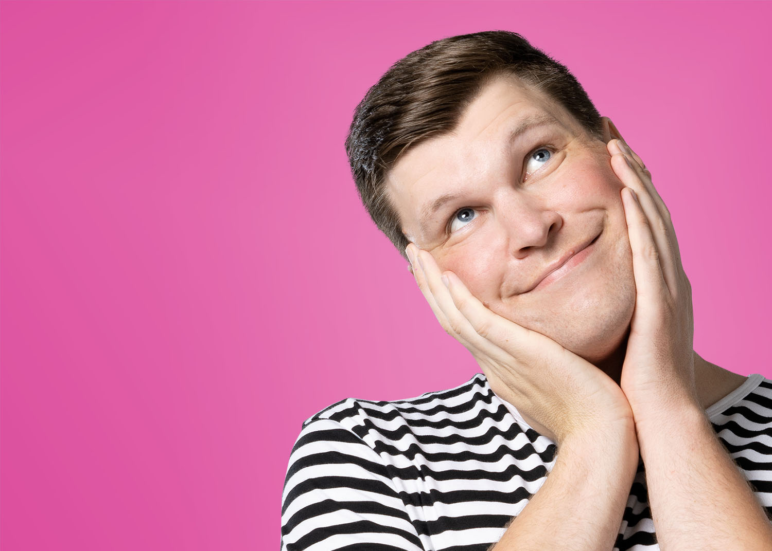 A photograph of me, Timo Lehtonen. I am a white male in my late twenties. In the picture, I am smiling and looking up with my hands around my head. I am wearing a black and white striped shirt against a colourful magenta background.